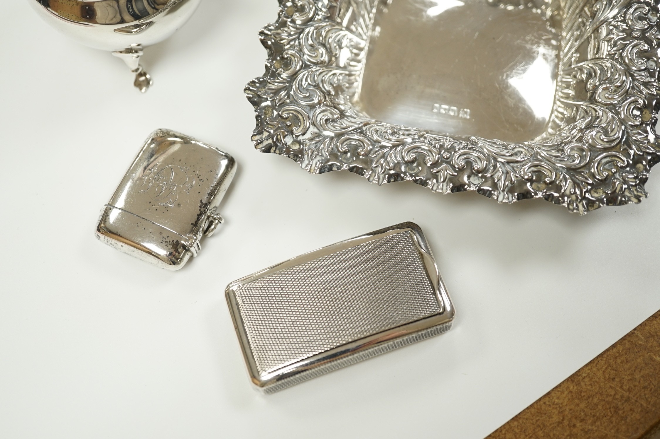 A small group of collectable silver including a repousse bonbon dish, 13.5cm, cigarette case, silver cream jug and sugar bowl, butter shell, vesta case, match sleeve, two apostle teaspoons and a George III curved silver